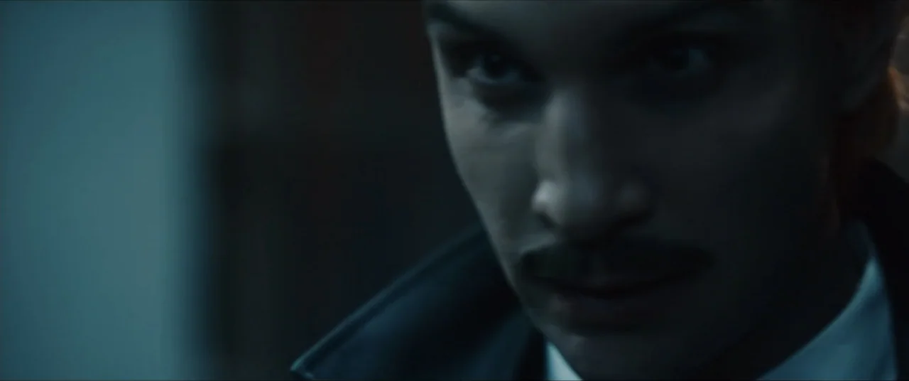 Vicious Fun (2021) movie still: closeup — A dark interior setting with minimal light sources casting deep shadows across the environment. A man in a…