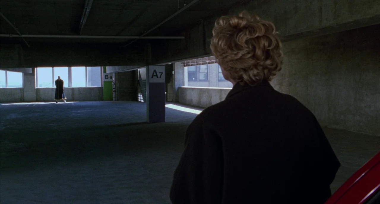 Candyman (1992) movie still: medium — A concrete parking structure features pillars labeled A7 and B6 under heavy shadows. A blonde woman looks…