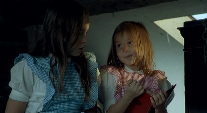 Bluebeard (2009) movie still: medium — A dimly lit room with high rafters and angled walls. Two young girls interact while holding a small red book…