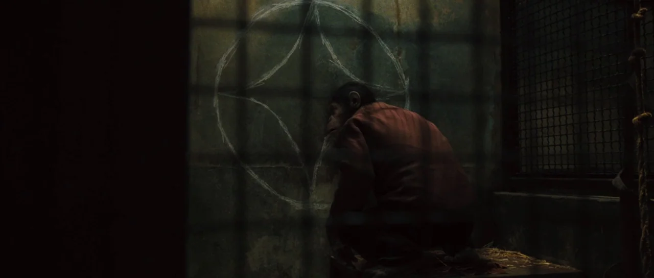 Rise of the Planet of the Apes (2011) movie still: medium — A dark, cramped concrete animal enclosure features a scratched circle symbol on the…