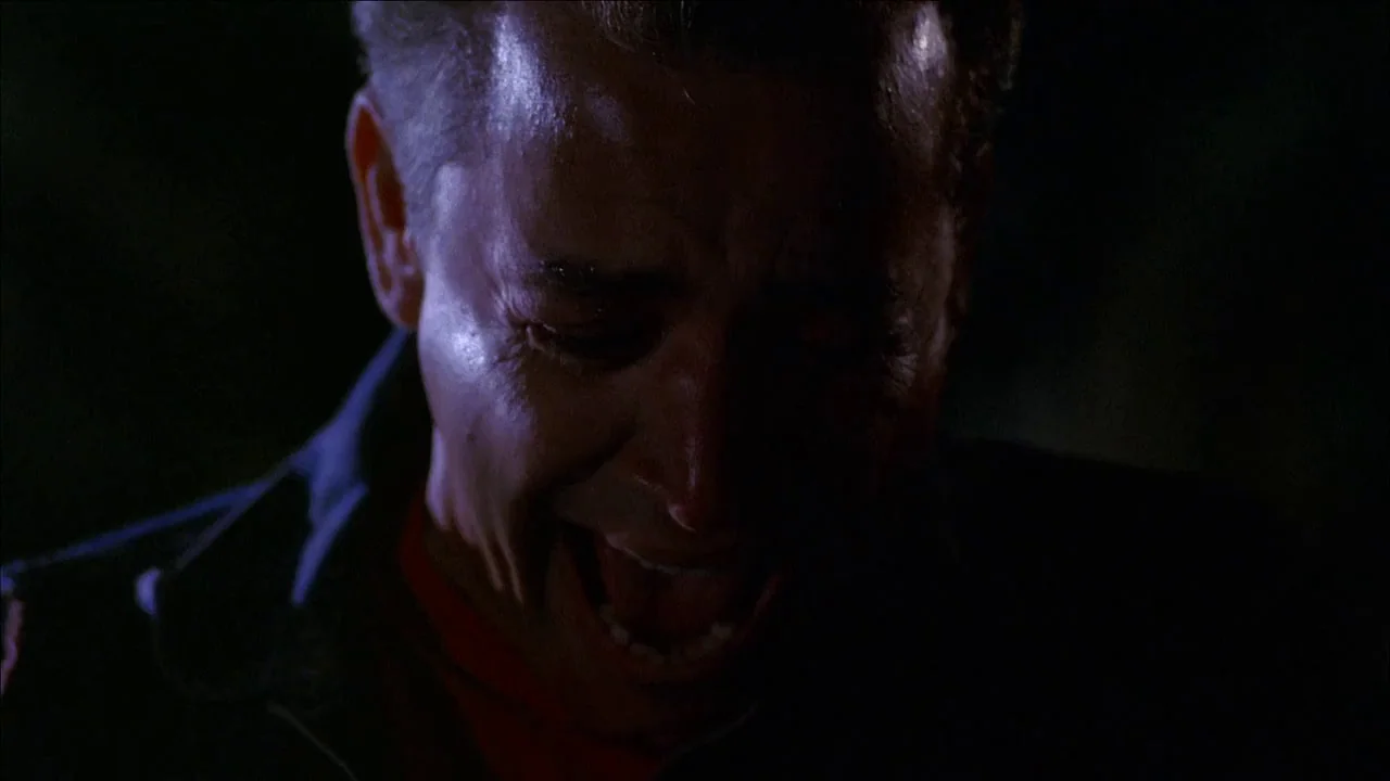 The Slumber Party Massacre (1982) movie still: closeup — A person is captured in a dimly lit, dark space with minimal background detail. The subject…