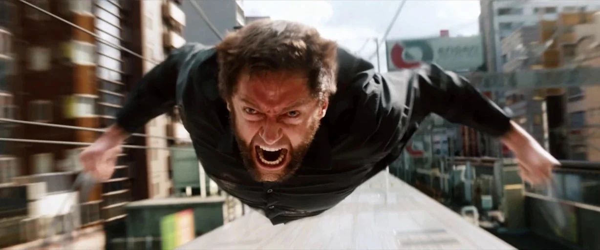 X-men (2000) movie still: closeup — A man lies prone on the roof of a high-speed train moving through Tokyo. The background shows blurred city…