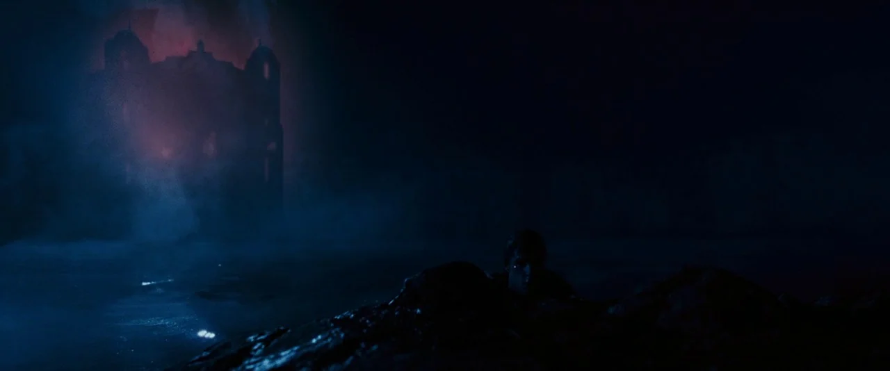 Dead Silence (2007) movie still: wide — A dark rocky coastline is shrouded in heavy mist under a night sky. A large, dimly lit gothic building looms…