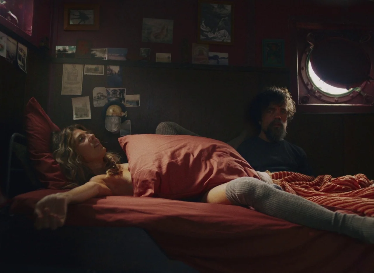 She Came To Me (2023) movie still: medium — A dimly lit boat cabin featuring wood-paneled walls decorated with various small framed photographs. A…
