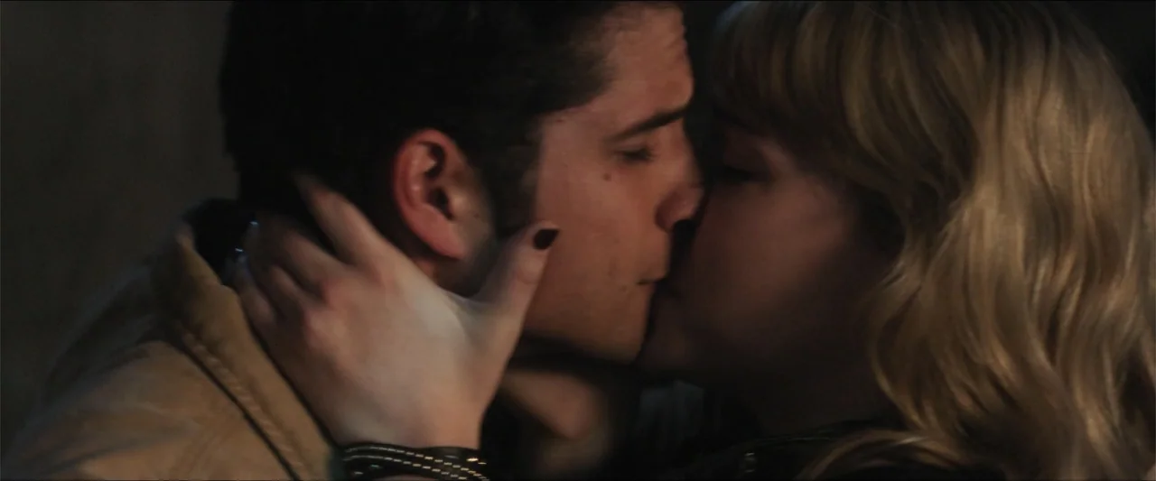 Truth or Dare (2018) movie still: closeup — An interior space provides a dimly lit background for the close interaction of two people. A young man…