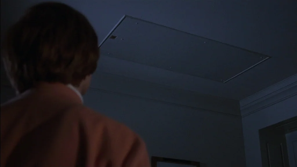 The Exorcist (1973) movie still: medium — An interior space features a dark ceiling with a rectangular access panel installed. A person stands in…