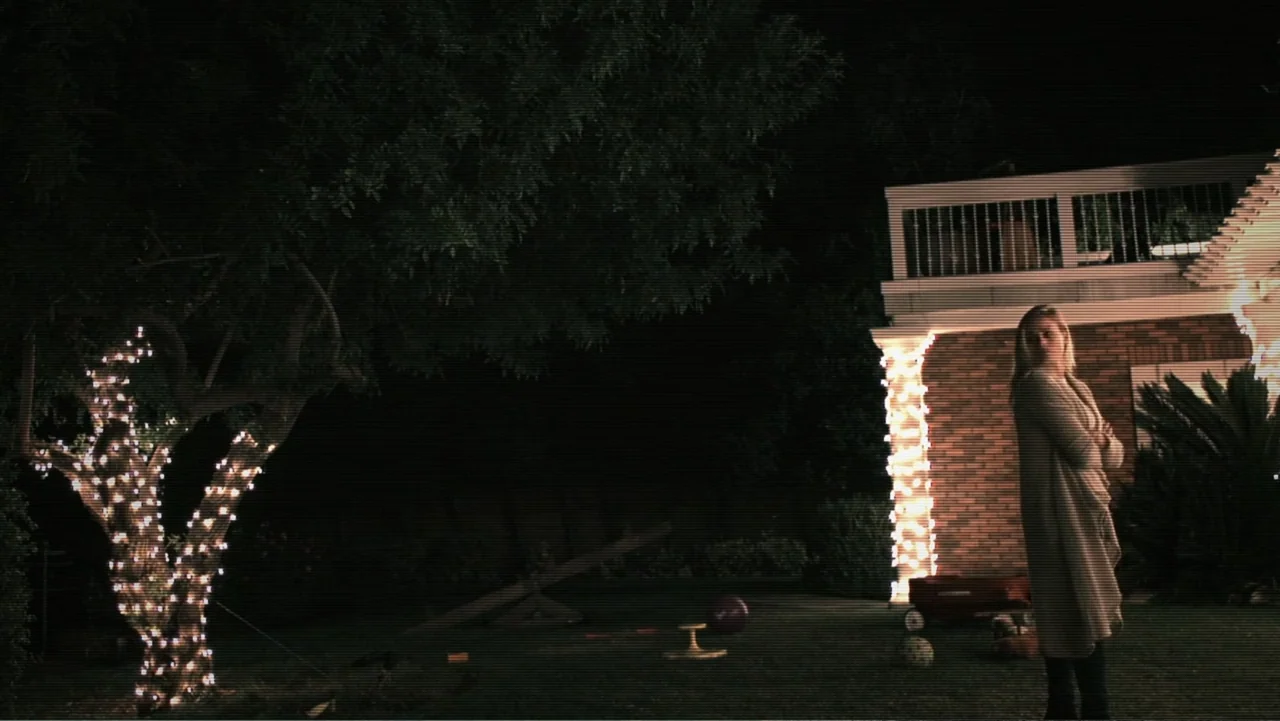 Paranormal Activity: The Ghost Dimension (2015) movie still: medium — A dark backyard at night features a tree and building illuminated by fairy…