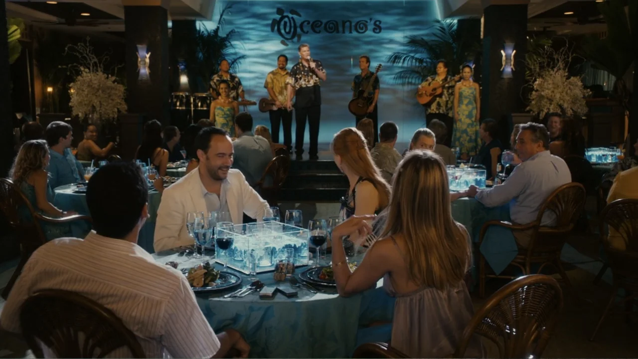 Just Go with It (2011) movie still: medium — A dimly lit upscale restaurant features a live band performing on a blue-lit stage. A man in a white…