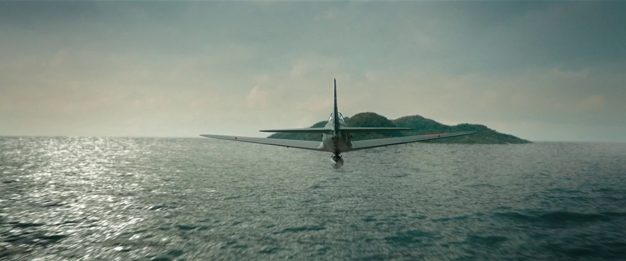 Godzilla Minus One (2023) movie still: wide — A dark military propeller plane flies low above the undulating blue ocean surface. An island landmass…