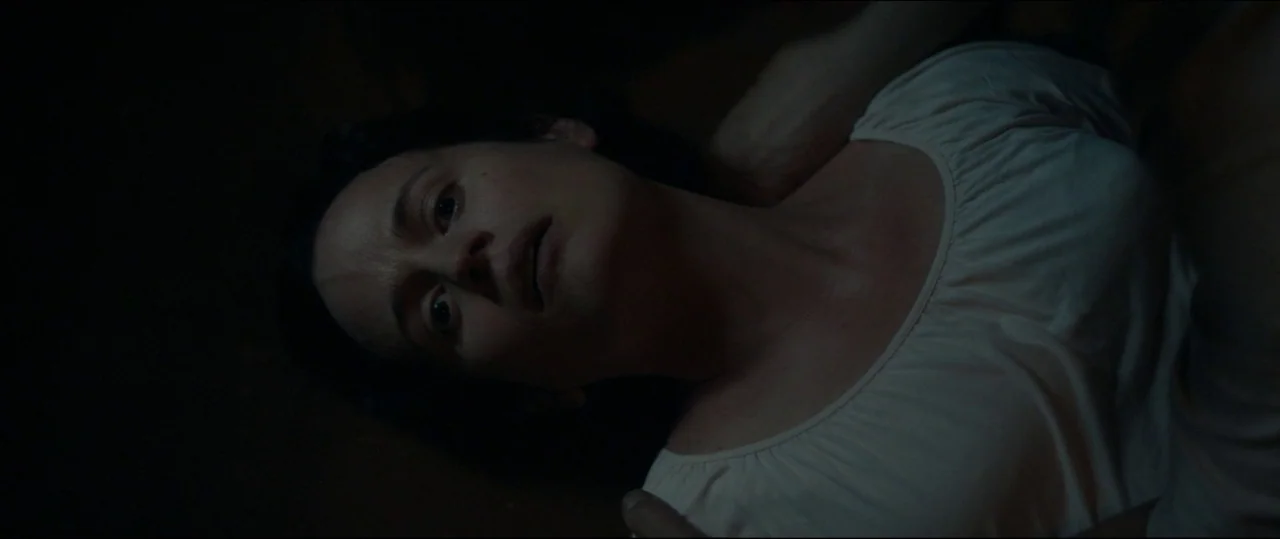 One & Two (2015) movie still: closeup — A dark environment with a woman lying supine on a surface. The woman gazes upward with a neutral expression…