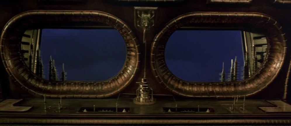 Dune (1984) movie still: establishing — A dark spaceship interior features two oval portals overlooking a futuristic, silhouetted city skyline.…