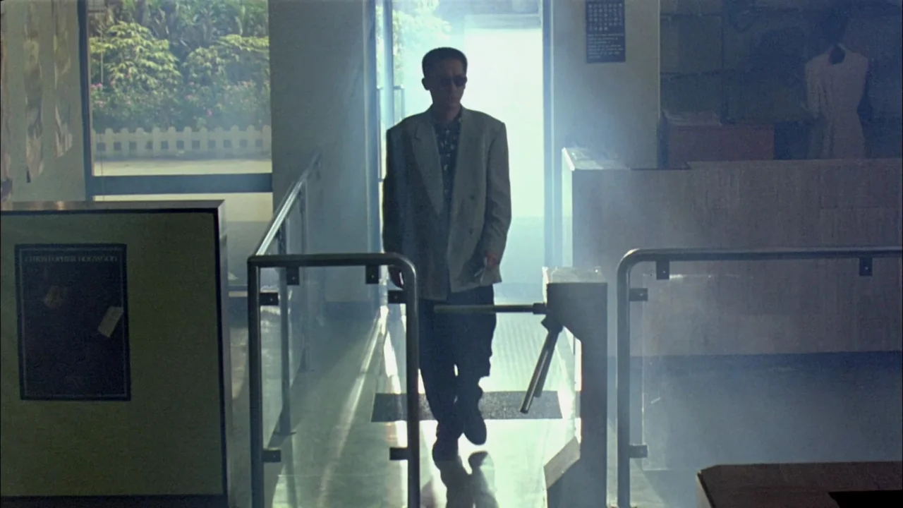 Hard Boiled (1992) movie still: fullbody — A bright office lobby features a turnstile entrance obscured by hazy, atmospheric smoke. A man in…