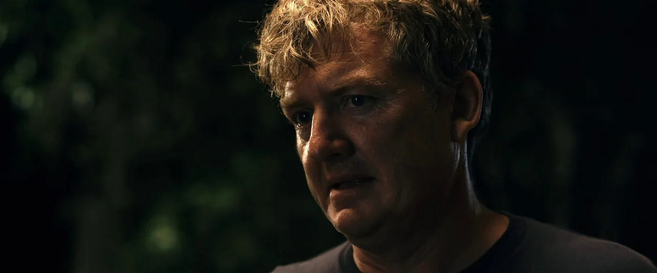 The Loved Ones (2009) movie still: closeup — A man stands in a dark forest at night surrounded by foliage. He faces partially away from the camera…