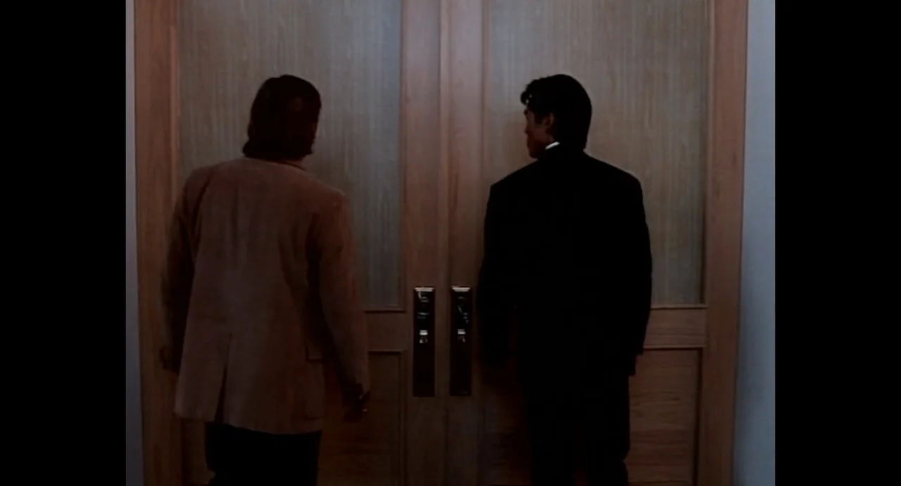 American Yakuza (1993) movie still: fullbody — A modern office interior features a set of double light wood doors. Two men stand facing the doors as…