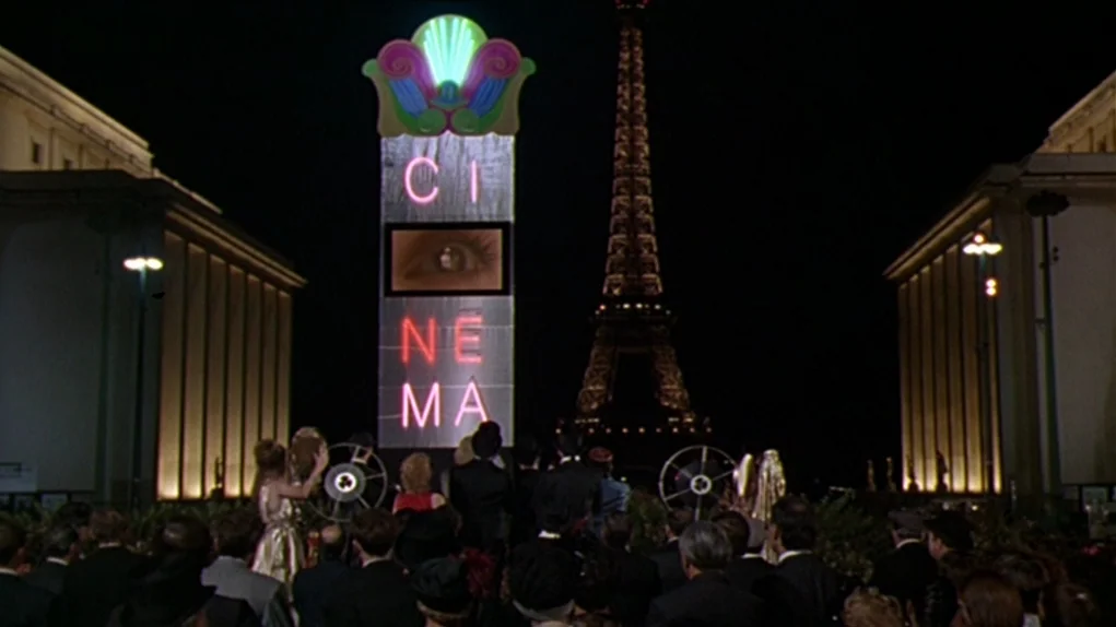 One Hundred and One Nights (1995) movie still: wide — A crowd gathers at night in a plaza with large neoclassical buildings on either side. A tall…