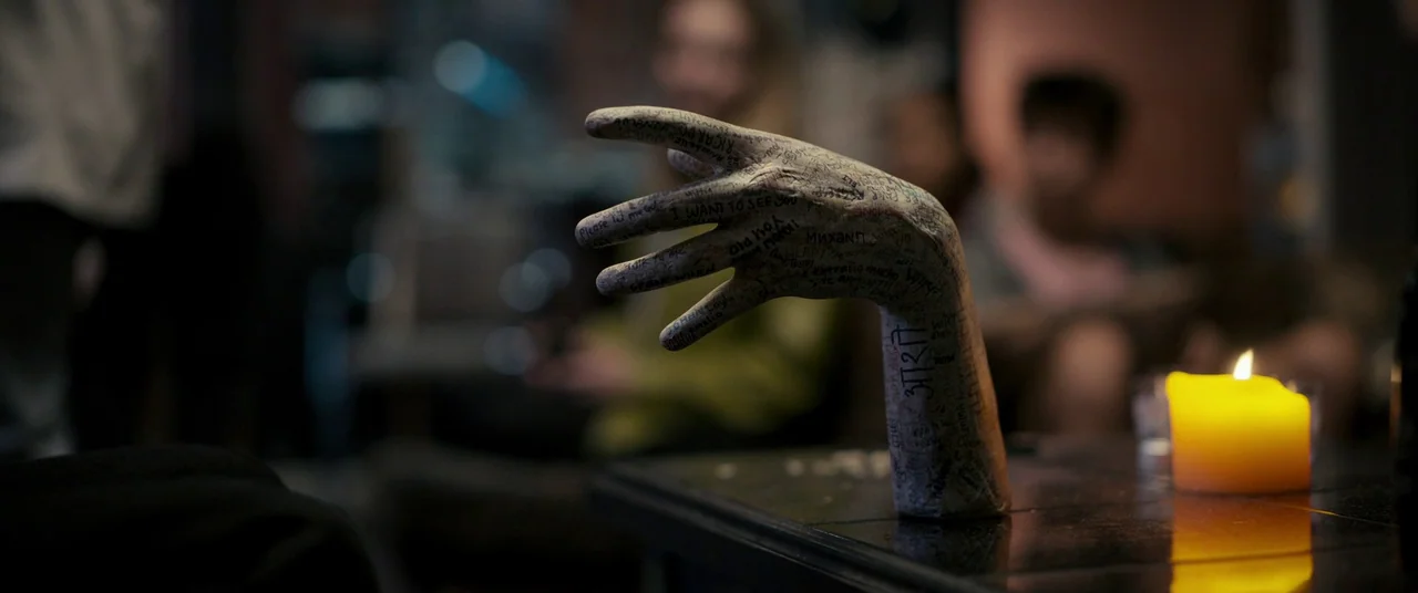 Talk To Me (2022) movie still: closeup — A dark indoor setting features a plaster hand sculpture covered in handwritten black ink. The hand stands…
