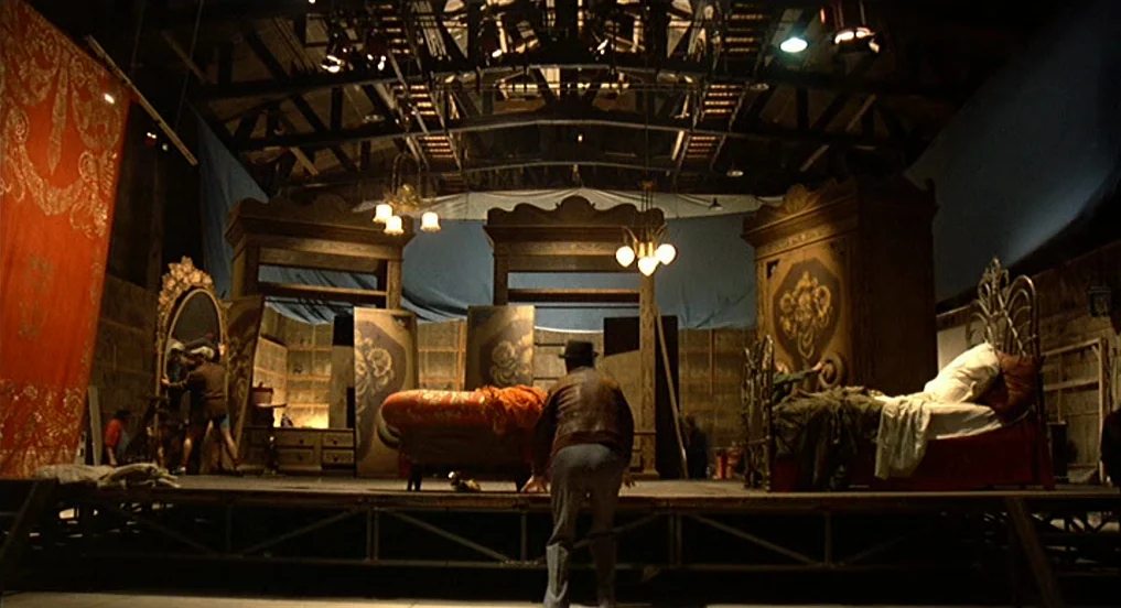 Intervista (1987) movie still: wide — A spacious industrial soundstage houses a large film set depicting a furnished bedroom. A man in a leather…