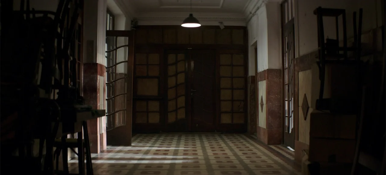 Morir un Poco (1967) movie still: wide — A dimly lit indoor corridor features patterned tile floors and ornate wooden paneled doors. The space…