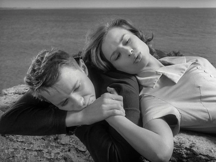 Through A Glass Darkly (1961) movie still: medium — A man and woman lie together on a rocky cliff overlooking the ocean. The two subjects rest their…
