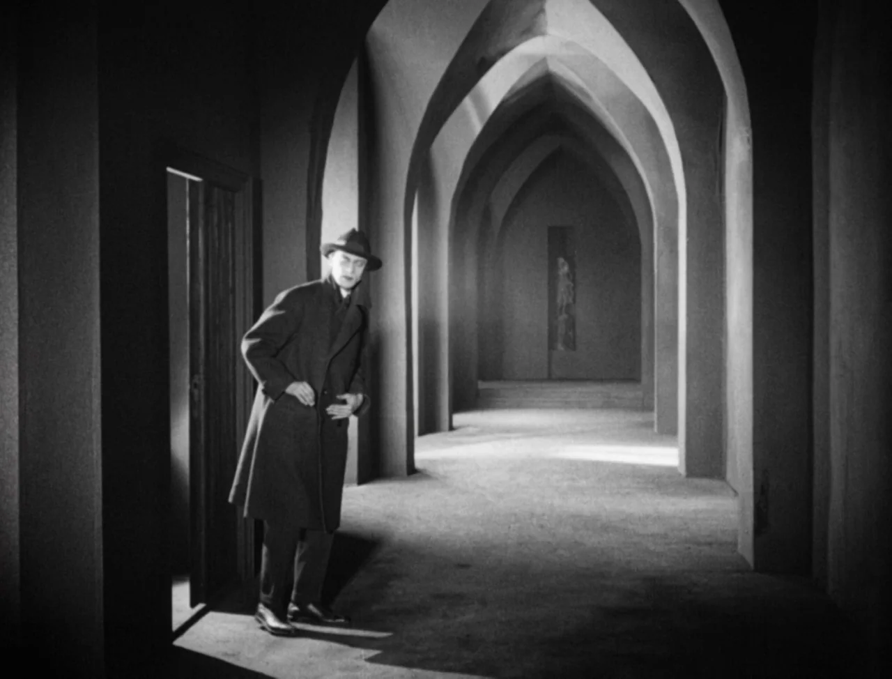 The Hands of Orlac (1924) movie still: fullbody — A long corridor features a series of pointed gothic arches creating rhythmic depth. A man in a…