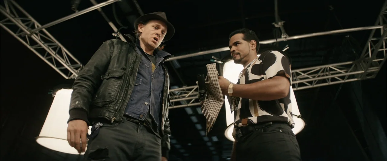 Last Looks (2022) movie still: medium — A high-ceiling industrial soundstage with exposed metal trusses and large white production light rigs. A man…