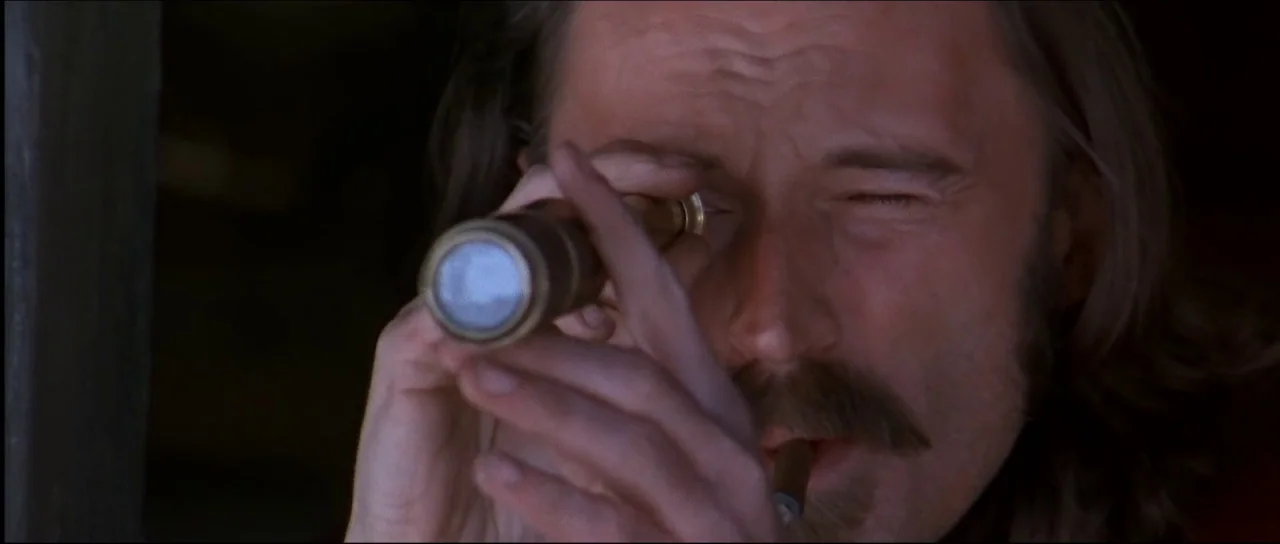 Ravenous (1999) movie still: closeup — A man looks through a brass telescope inside a dimly lit wooden structure. He holds the telescope with one…