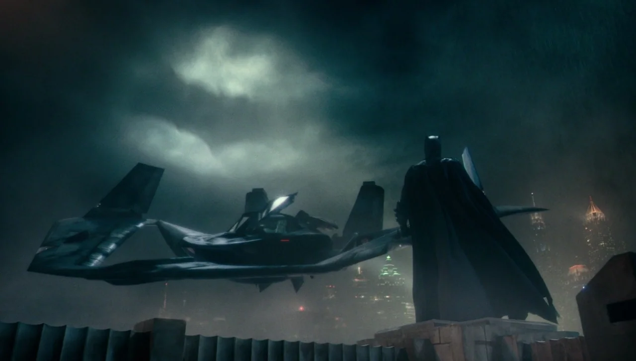 Justice League (2017) movie still: wide — A dark, misty rooftop overlooking a hazy urban skyline under a heavy cloudy sky. A caped figure stands on…