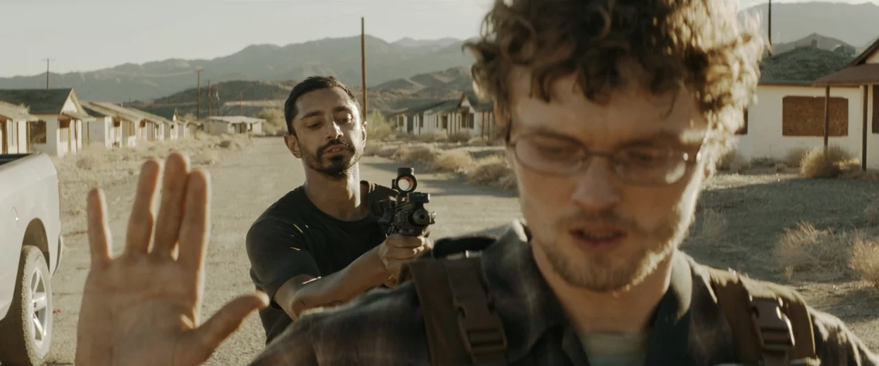 Encounter (2018) movie still: medium — A desolate road in an abandoned desert location with small buildings in the distance. One man stands behind…