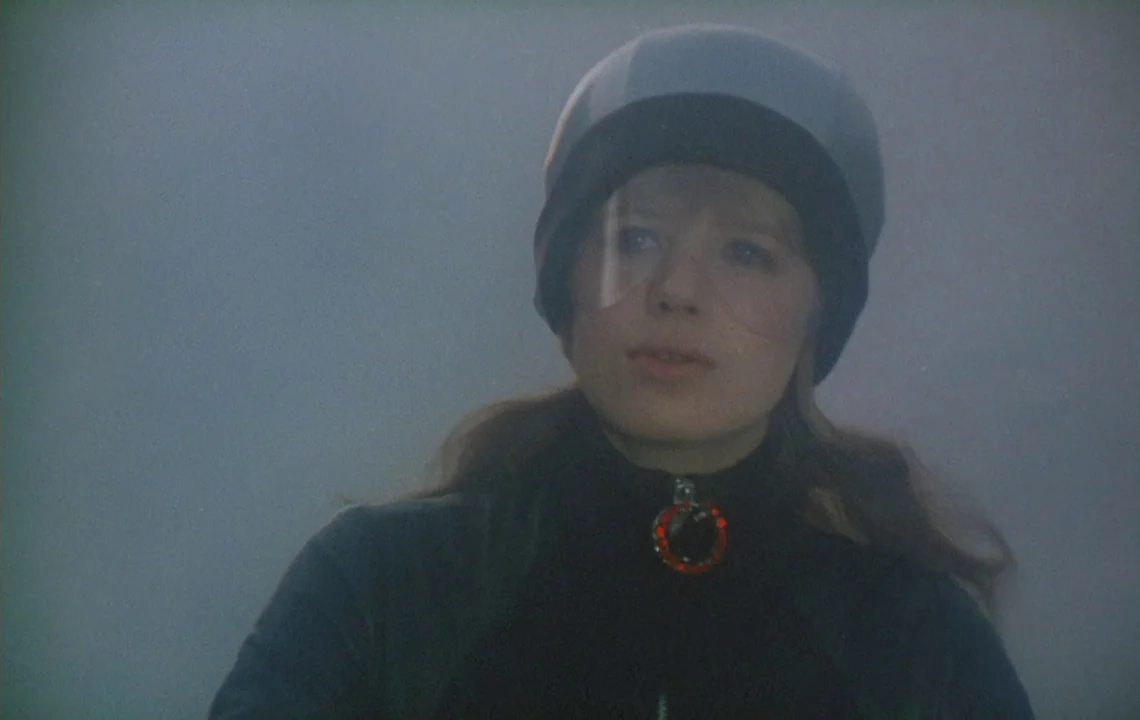The Girl on a Motorcycle (1968) movie still: closeup — A woman stands in a vast, foggy, overcast outdoor environment during daylight hours. She…