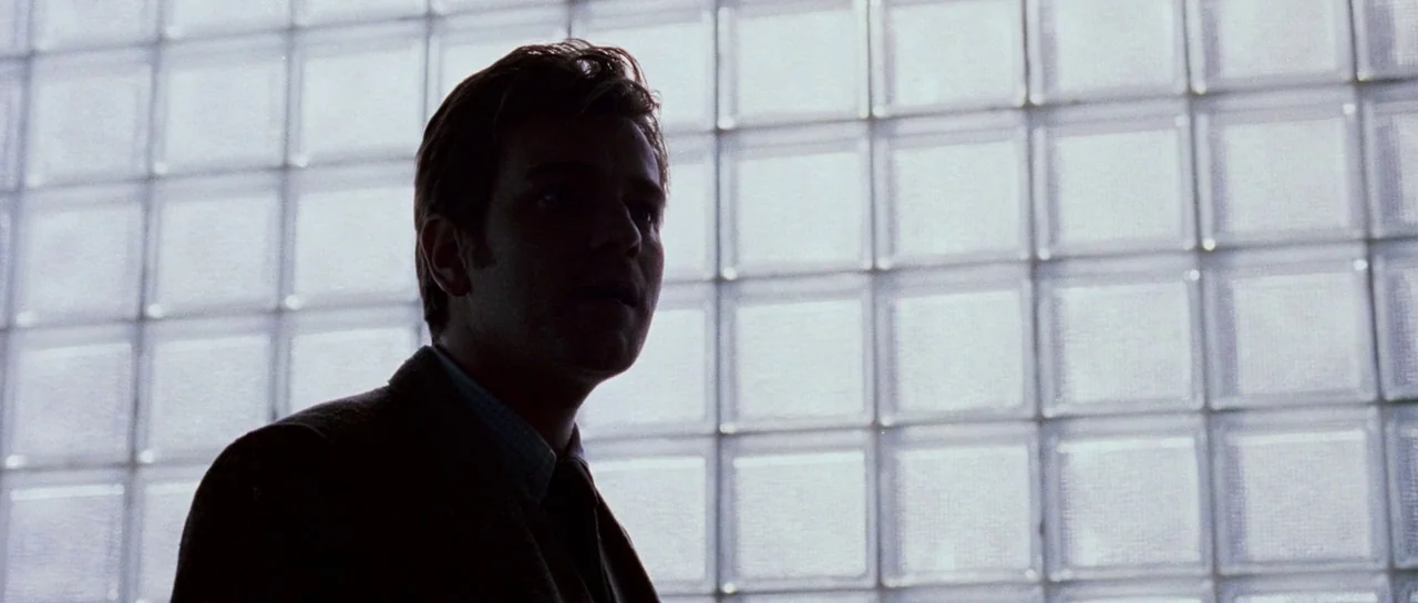 Stay (2005) movie still: medium — A wall constructed of modular glass blocks provides a bright, grid-like backdrop. A man stands in the foreground,…
