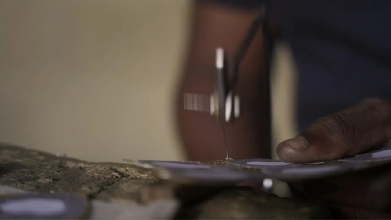 Victoria's Secret: The Tour '23 (2023) movie still: closeup — A workbench surface holds a thin piece of metal being shaped by a saw. A human hand…