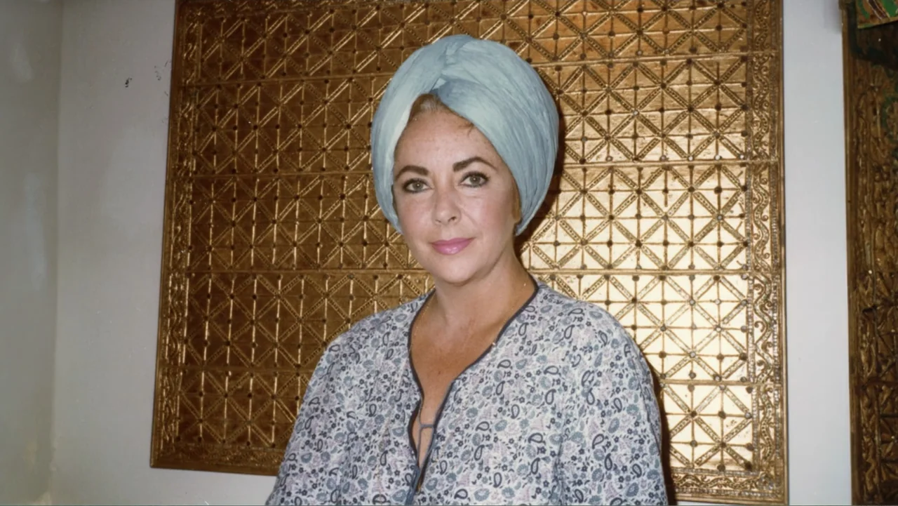 Elizabeth Taylor: The Lost Tapes (2024) movie still: medium — A woman stands before a large rectangular gold-leaf wall panel with a geometric…