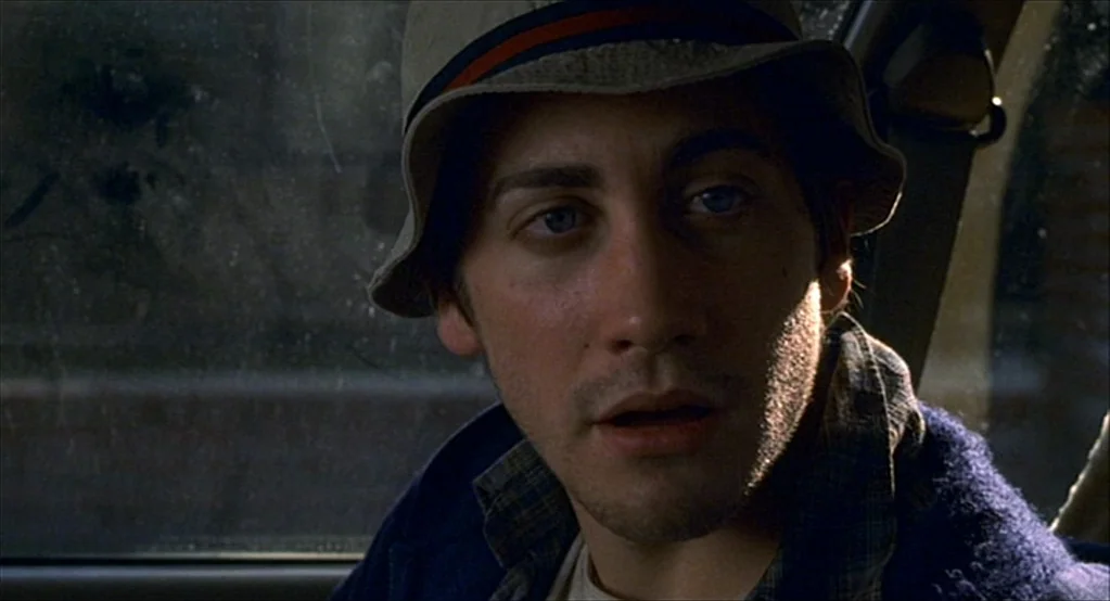 The Good Girl (2002) movie still: closeup — Inside a vehicle, a man sits in the passenger seat beside a dusty window. The man looks toward the side…