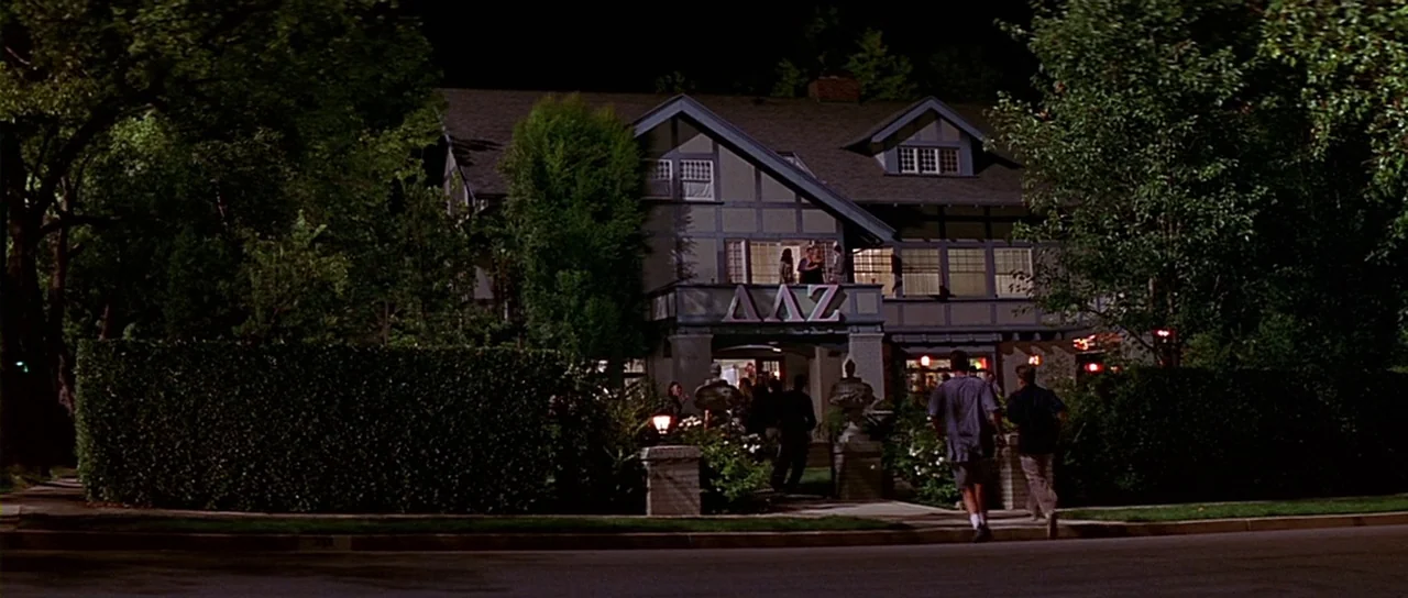 Scream 2 (1997) movie still: wide — A two-story Tudor-style house with Greek letters on the facade sits at night. Two young men approach the front…