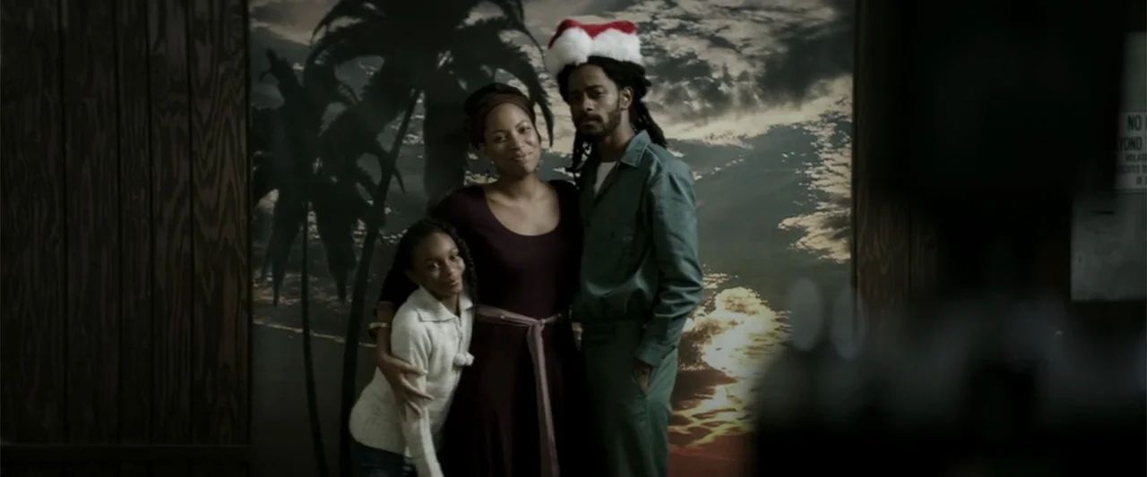 Crown Heights (2017) movie still: medium — A studio space features a palm tree backdrop with three people posed for portraits. An adult man wearing…