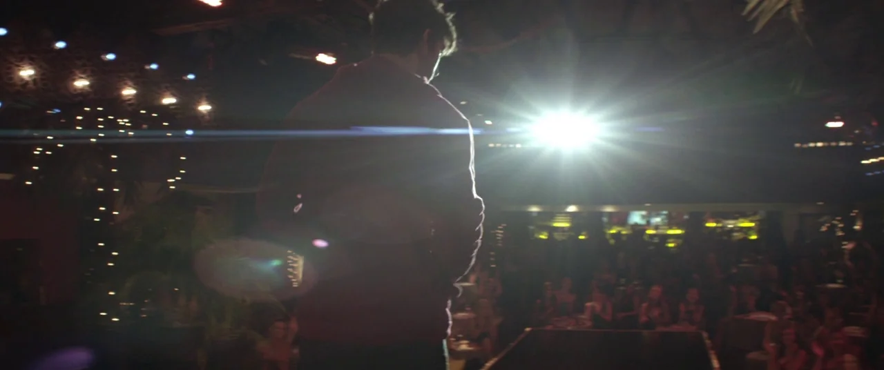 Magic Mike (2012) movie still: medium — A dark, dimly lit venue features a person standing on a stage platform. They face a crowd partially visible…
