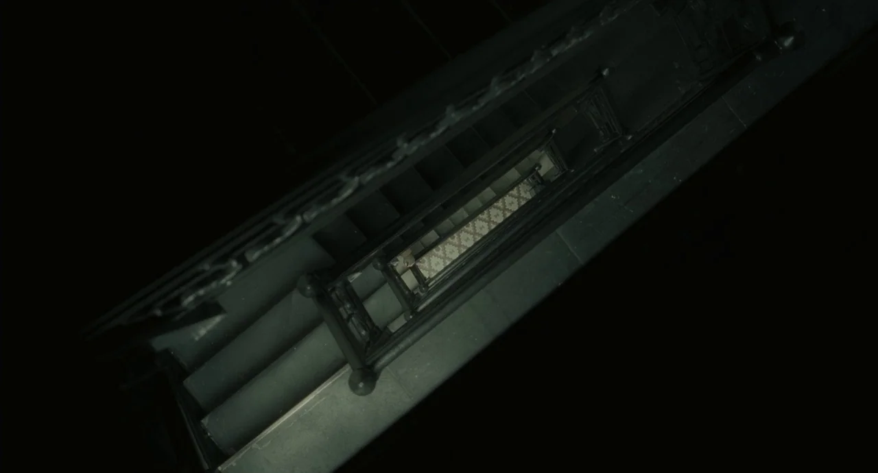 Inside Llewyn Davis (2013) movie still: wide — An overhead view looks directly down a dark, narrow staircase with ornate metal railings. A patterned…