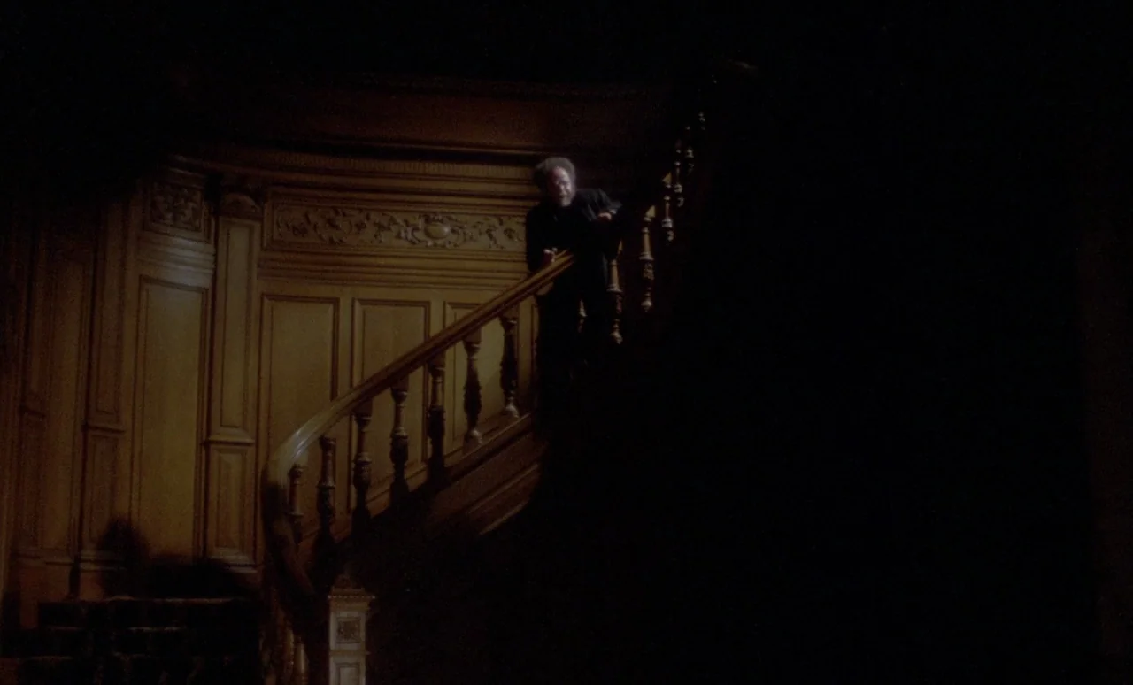 The Strange Case of Dr. Jekyll and Miss Osbourne (1981) movie still: wide — A dimly lit wooden staircase features intricate carvings on the wall…