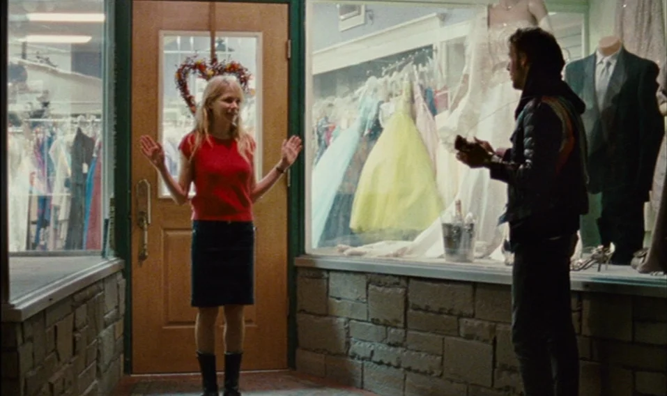 Blue Valentine (2010) movie still: fullbody — A formal wear store features a display window filled with dresses and mannequins. A woman stands in a…