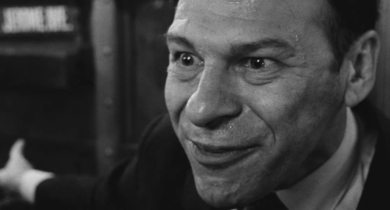 The Incident (1967) movie still: closeup — A dark, cramped interior setting with metallic textures visible behind the subject. A man in a suit looks…
