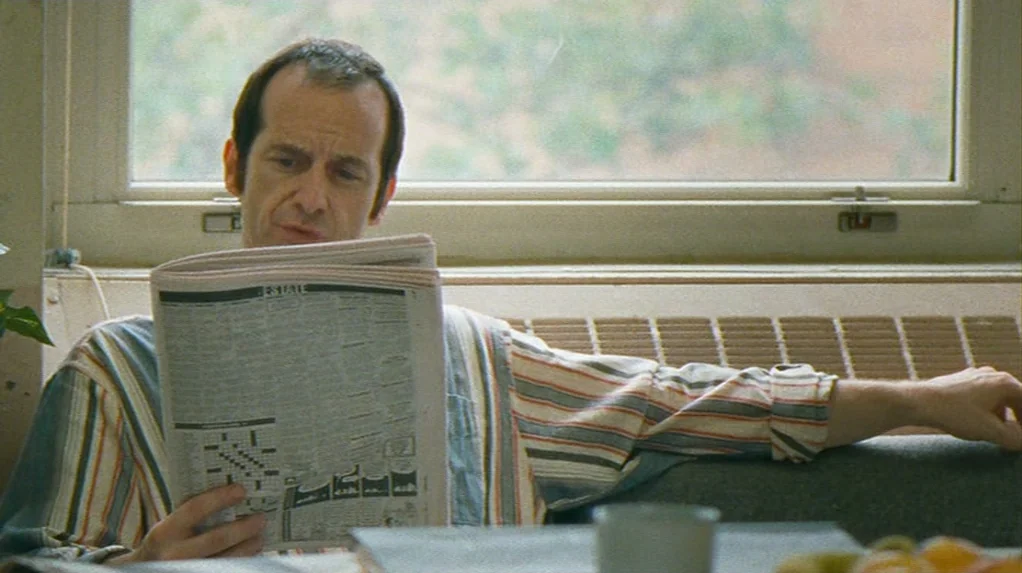 Half Nelson (2006) movie still: medium — A man sits on a couch in front of a window in a room. He reads a newspaper while holding it in both hands.