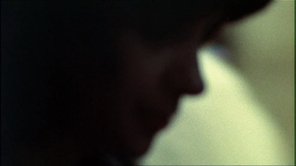 The Conversation (1974) movie still: closeup — A dark, out-of-focus indoor space contains a partially obscured person. The subject stands with their…