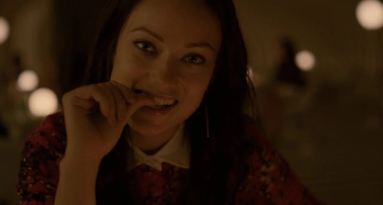 Her (2013) movie still: closeup — A dimly lit interior space features blurry spherical lamps illuminating the dark background. A woman smiles while…