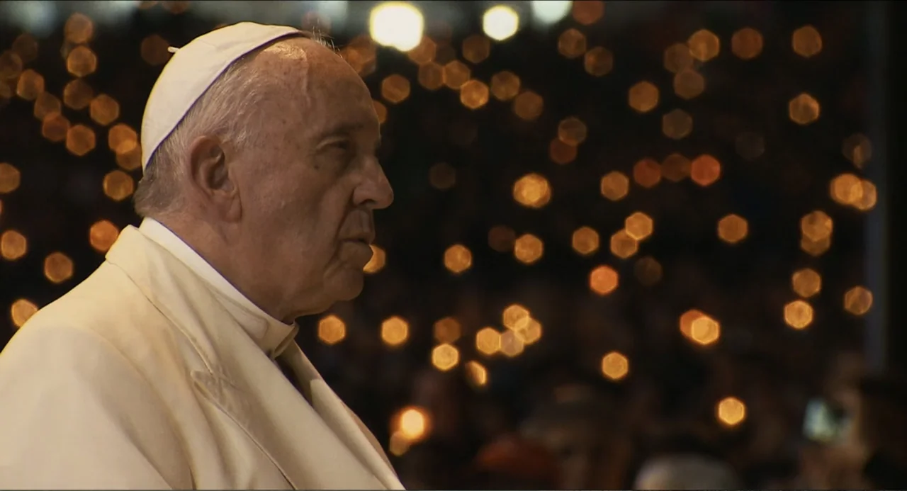 Pope Francis: A Man of His Word (2018) movie still: closeup — A night setting in a large public space with numerous blurred candle-like lights in…