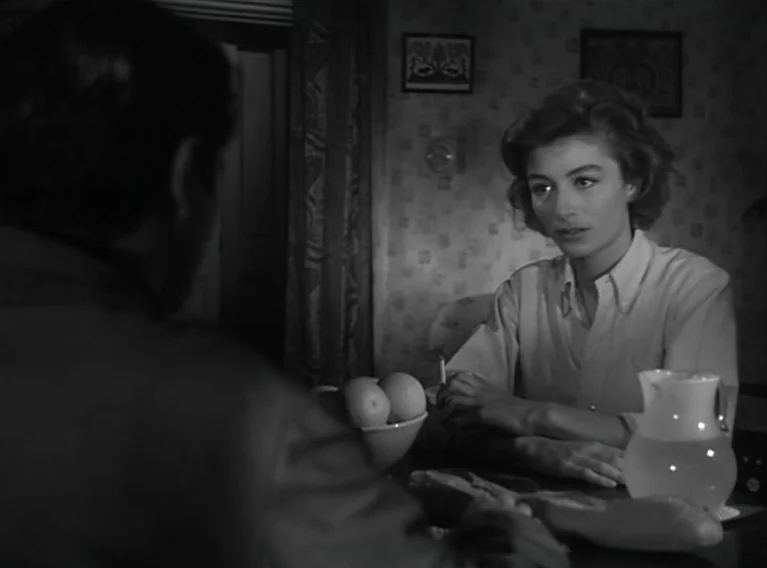Head Against The Wall (1959) movie still: medium — A dark dining room with patterned wallpaper features a woman seated at a table. She sits opposite…