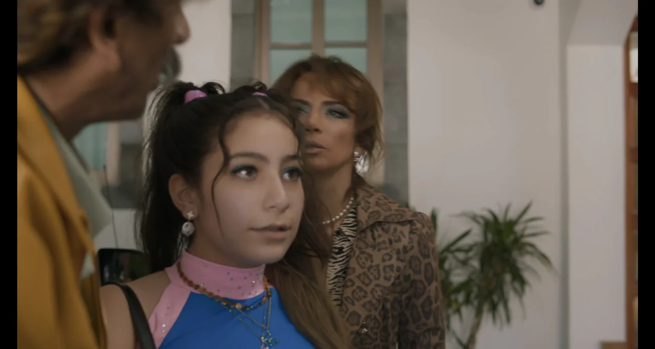 National Family (2023) movie still: medium — A well-lit interior space features white walls and a glimpse of a potted plant. A teenage girl in a…