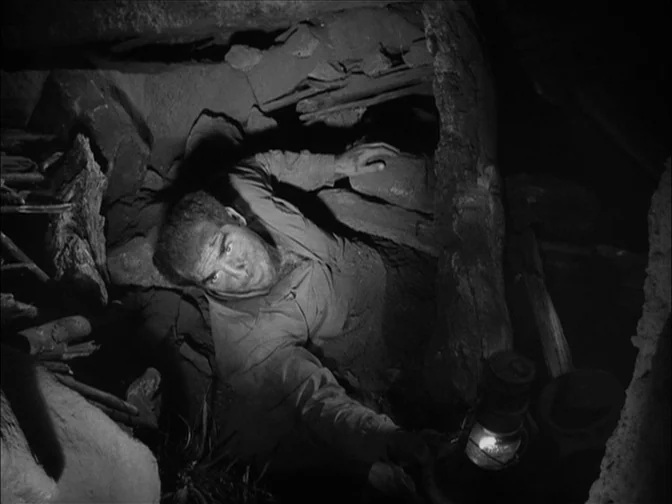 Ace In The Hole (1951) movie still: medium — A cramped, dark underground passage features dirt walls reinforced with rough wooden planks. A man…