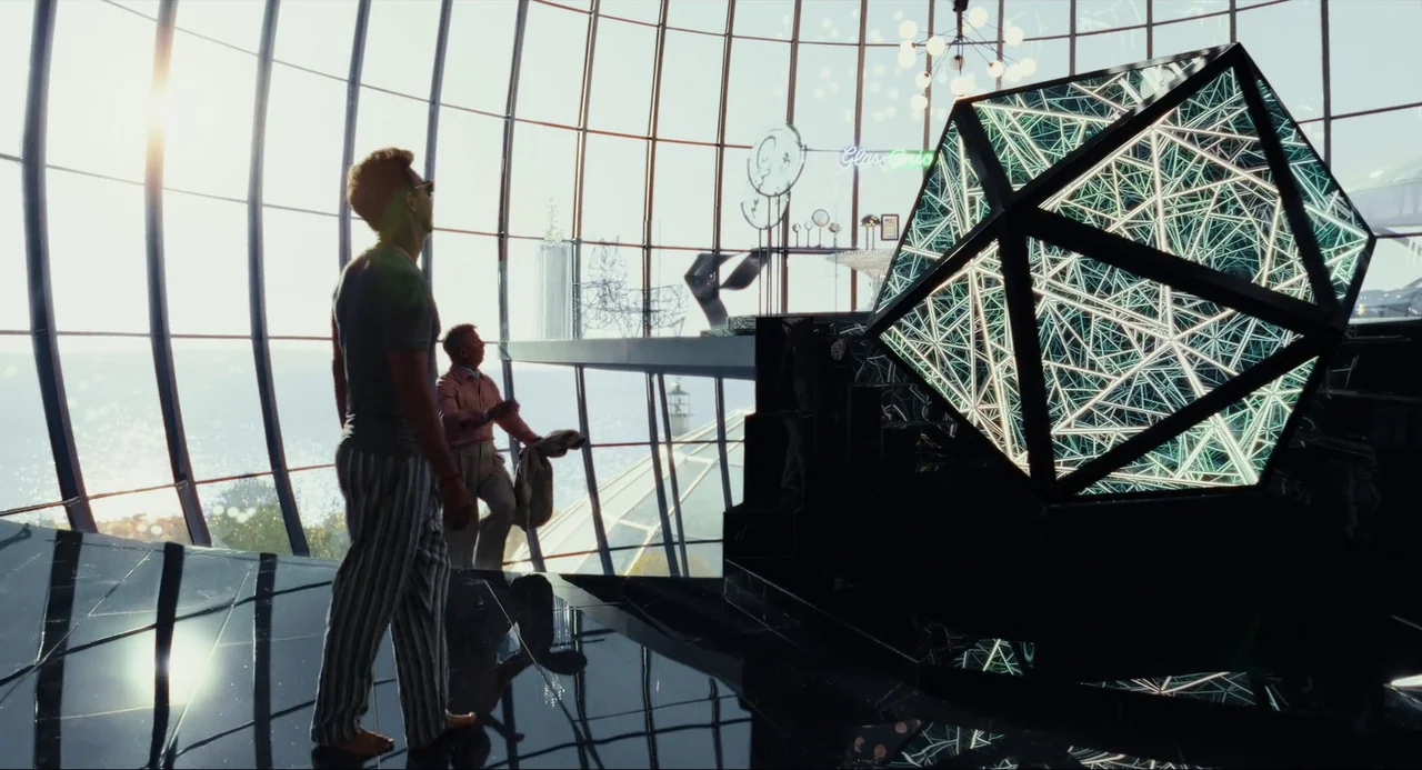 Glass Onion (2022) movie still: wide — A spacious, glass-domed architectural interior overlooks the ocean during the daylight hours. Two men walk…