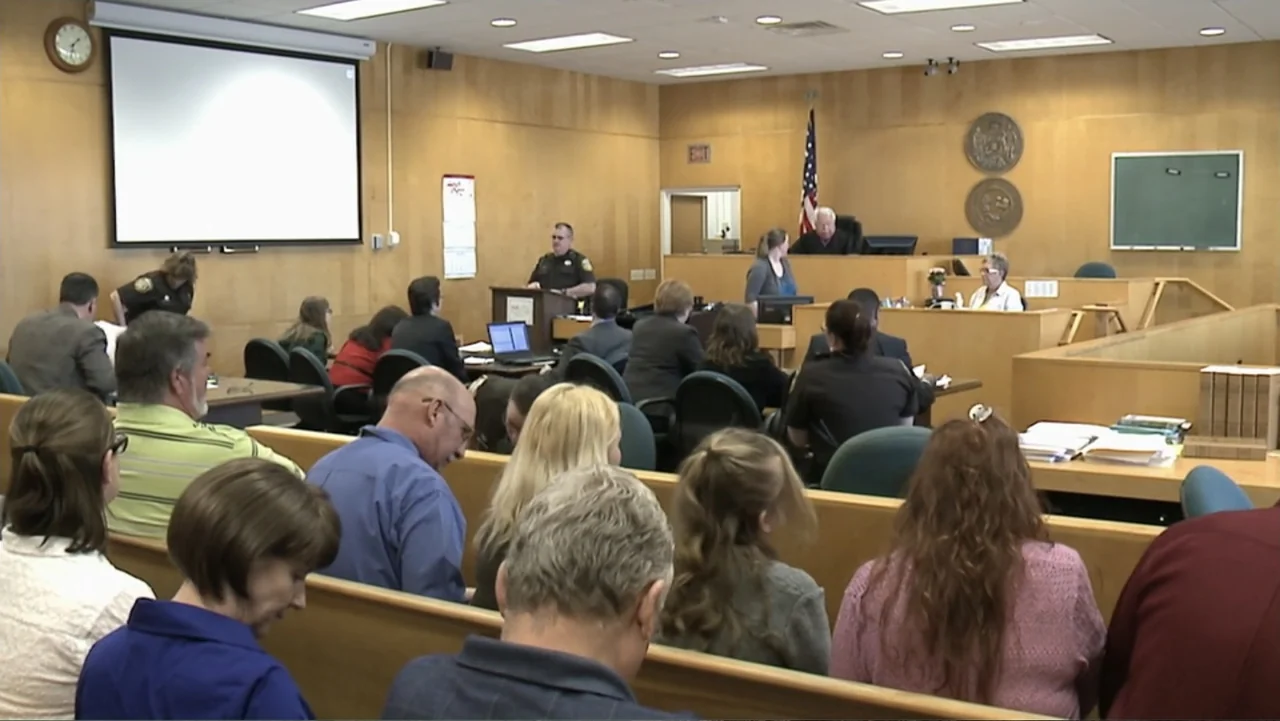 Beware the Slenderman (2016) movie still: wide — A wood-paneled courtroom filled with seated spectators and legal personnel. The judge sits at the…