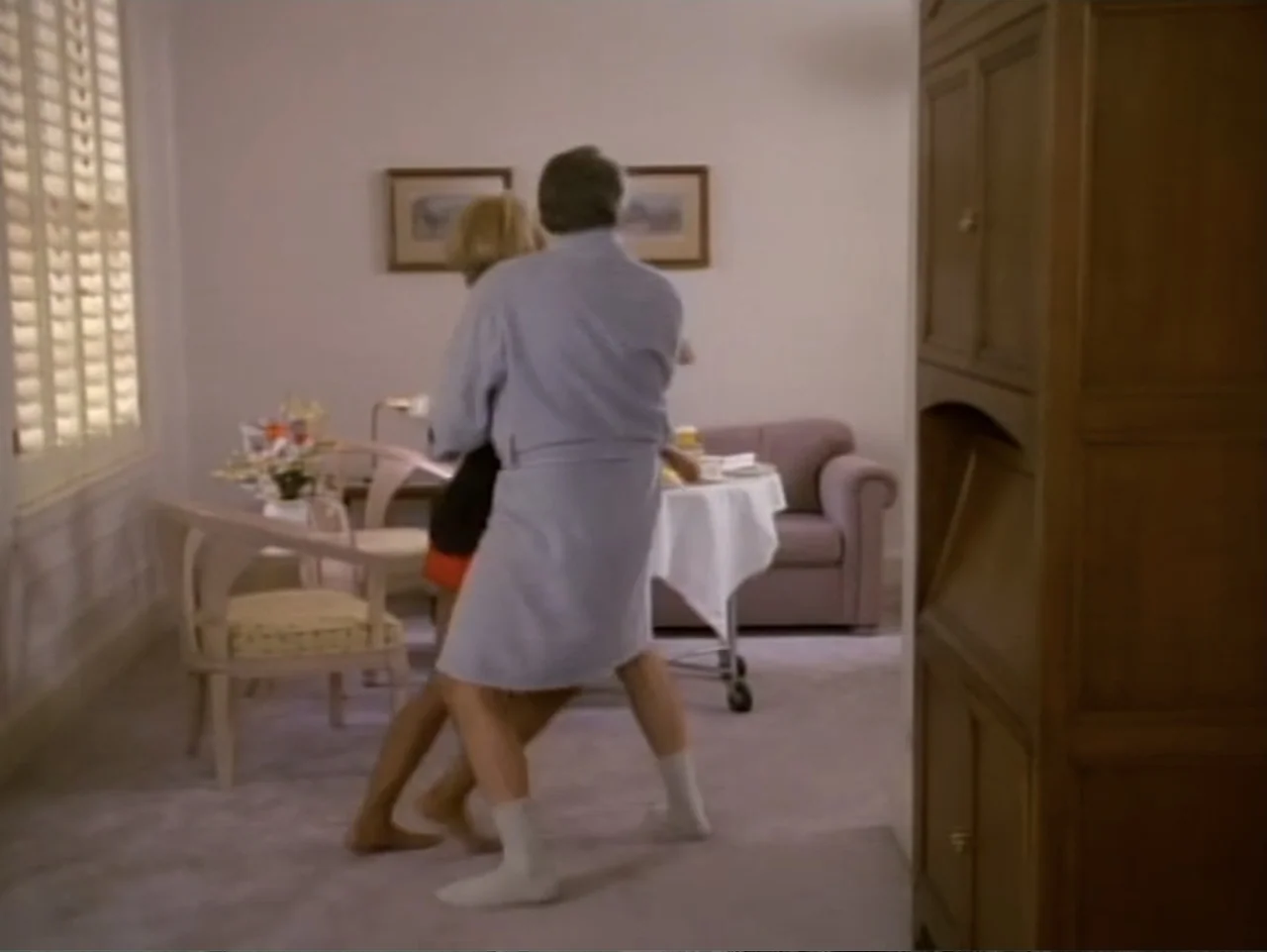 My First Love (1988) movie still: fullbody — An interior hotel room features beige carpet, wooden furniture, and two framed wall pictures. A man and…
